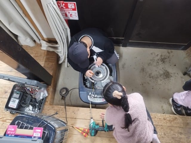 3人、給湯器、グラインダー、、「火器 火 AT 来 몸음 IA - noA ባት」というテキストの画像のようです